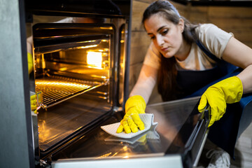 Woman cleaning oven with gloves inside modern kitchen during day