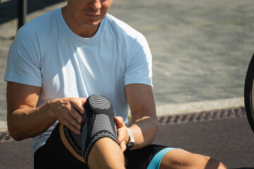 Cyclist fell off his bike and injured his knee. Unhappy cyclist with knee pain and injury outdoors. Close up.