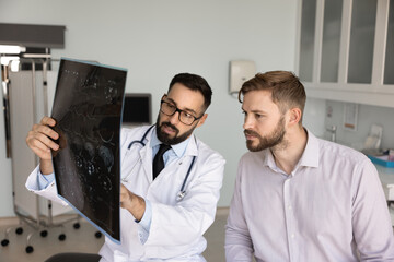 Serious Hispanic medical practitioner explaining X-ray to young male patient in hospital...
