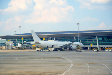 A large airplane is parked on the tarmac next to a sleek airport terminal. Ground crews are...