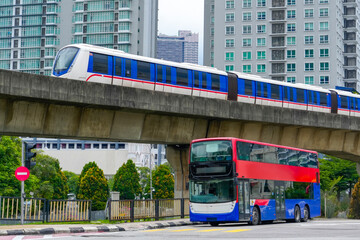 A futuristic monorail glides above a red and blue double-decker bus stopped at a traffic light in a...