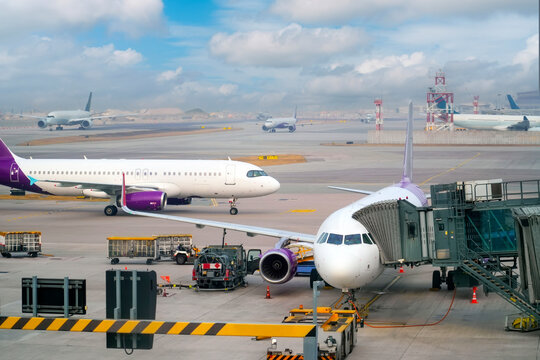 Several aircraft, including commercial jets and cargo planes, are positioned on the tarmac of a busy airport during daylight, with a blue sky and scattered clouds above