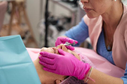 Beautician injecting filler into nose of woman lying on table