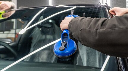 Automobile special workers replacing windscreen or windshield of a car in auto service station...