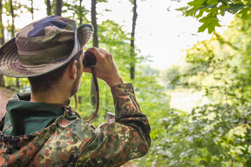 Soldier wearing camouflage uniform observing with binoculars in forest