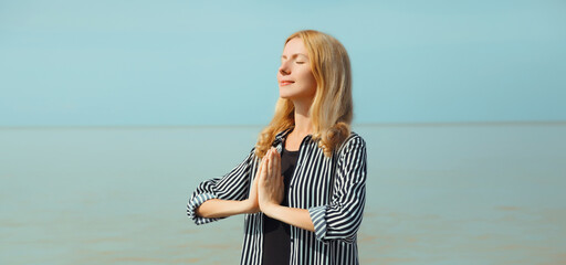 Calm relaxing healthy young woman meditates, happy girl practicing yoga on the beach on sea