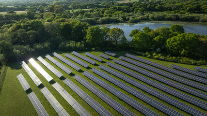 An expansive solar panel farm nestles in the green, serene landscape by a sparkling lake.