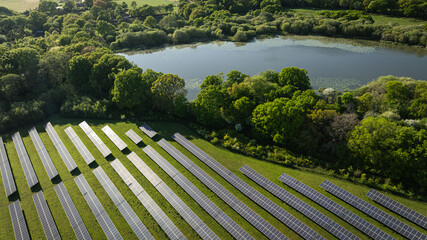 An expansive solar panel farm nestles in the green, serene landscape by a sparkling lake.