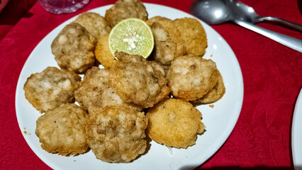 Golden-brown, crispy fried seafood or shrimp balls served on a white plate with a slice of fresh lime. The red tablecloth adds a vibrant contrast enhancing presentation
