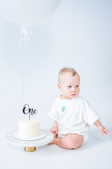 Baby celebrating first birthday with cake and balloon on white background. 