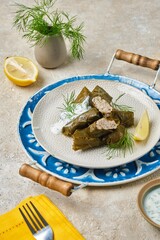 Dolma in grape leaves with minced meat, rice and spices on a light plate on a round tray on a light concrete background. Turkish, Azerbaijani cuisine.