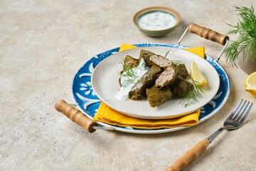 Dolma in grape leaves with minced meat, rice and spices on a light plate on a round tray on a light concrete background. Turkish, Azerbaijani cuisine.