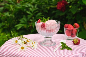 Three scoops of creamy strawberry ice cream with fresh strawberries in a glass bowl on a table with a tablecloth in the yard. Summer desserts.