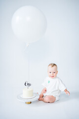 Baby celebrating first birthday with cake and balloon on white background. 