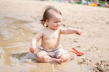 joyful toddler playing on a sandy beach, exploring wet sand and shallow water, depicting carefree childhood amidst a backdrop of warm sunlight and natural surroundings. moment, environment, focus