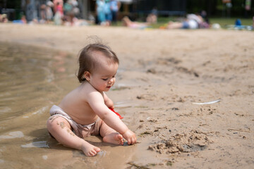 a joyful toddler plays on a sandy beach, exploring the water's edge with curiosity on a sunny day,...