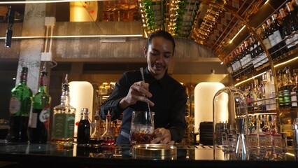 Smart Asian bartender using stirring mixed alcohol syrup into glass with ice for on the rock served...