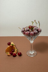 Frozen cherries in cocktail glass, ice cream cone, and brown background. Still life