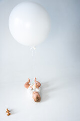 Baby lying on floor holding large white balloon with wooden toy nearby. 