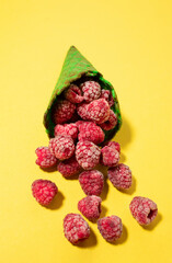 Frozen raspberries in green ice cream cone, on yellow background. Vibrant food photography. Flat lay