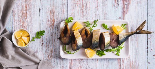 Smoked mackerel, lemon slices and herbs on a plate on the table top view web banner