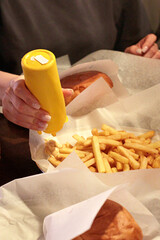 Closeup of hands adding mustard to french fries in a paper tray. Tasty fast food moment at a cozy...