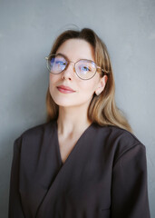 Portrait of a female healthcare professional in medical uniform and eyeglasses standing against gray wall.