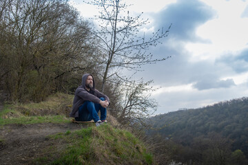 Man sitting quietly on a hillside contemplating nature during a cloudy day near a valley