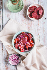 Chorizo ​​sausage, tomatoes and onion salad on a plate on a table top and vertical view