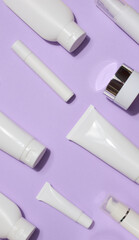 A variety of white plastic tubes and bottles with cosmetics arranged randomly on a lavender...
