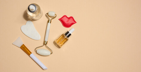 Set of cosmetics and skin care tools including facial massagers, decorative lips and serum bottles placed on beige background.
