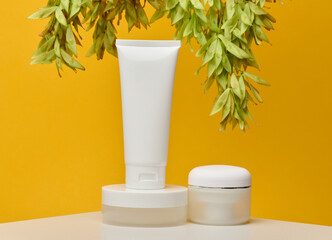 Three white cosmetic products without labels tube, flat round jar and short round jar, stand on white table against bright yellow background