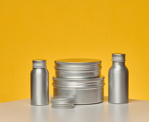 Aluminum jars and bottles for cosmetics and care. Minimalistic packaging on a bright yellow...