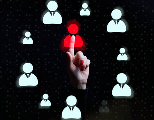 Female hand pointing at one red highlighted user icon among many blue icons on black background,...