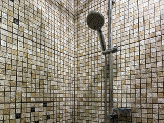 Shower stall with mosaic tiles, a chrome shower head, and a glass shelf. The neutral tones create a...