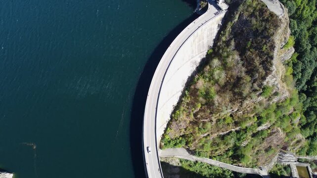 4K aerial footage of Vidraru Dam and Lake in Romania with a car crossing the dam on a sunny summer day