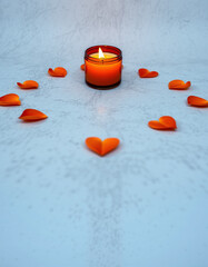 A small lit red candle surrounded by orange heart-shaped decorations on a snowy surface, creating a warm and romantic atmosphere suitable for love or memorial themes