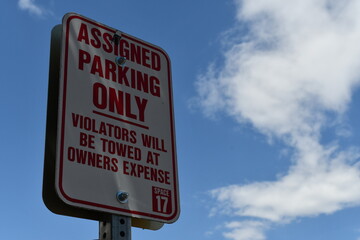 Assigned parking only sign. Violators will be towed by owners expense. Beautiful blue sky with...