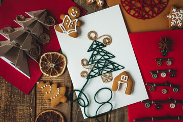 Flat lay. Preparation for a holiday season. Handmade children's greeting postcards with embroidered, origami fir tree, gingerbread cookies. Recyclable materials, eco friendly gift. Wooden background.