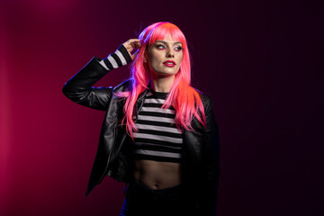 Young fashionable female with pink bangs hairstyle and eyeliner stands confidently with edgy outfit...