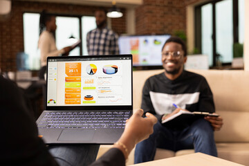 African american entrepreneur holding laptop showing company analytics, reviewing marketing...