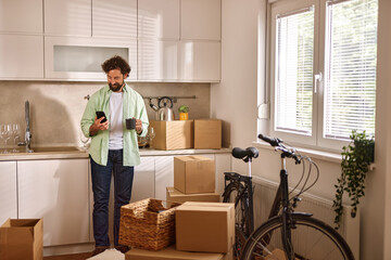 Man organizes his belongings in the kitchen of a new home while checking his phone for details...