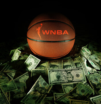 Raleigh, NC - USA - 04-15-2024: Basketball with WNBA logo on a pile of money on dark background