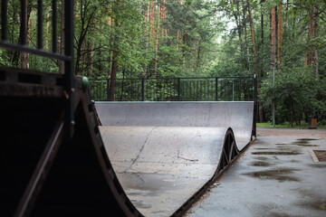 The concrete ramp skate is ready for action in a calm park surrounded by lush greenery and a metal...