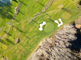 Aerial view of a lush golf course showcasing fairways and bunkers. The greens are surrounded by...