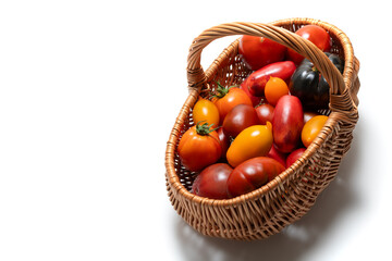 Wicker basket filled with colorful fresh tomatoes on a white background. A variety of tomato types including red, yellow, orange. Concept of organic vegetables, healthy eating, and farm produce.