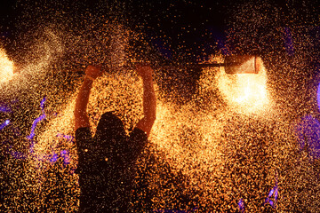 A dramatic silhouette of a fire performer wielding a flaming staff, surrounded by golden sparks in...