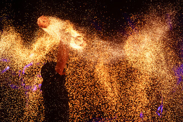 A dramatic silhouette of a fire performer wielding a flaming staff, surrounded by golden sparks in...