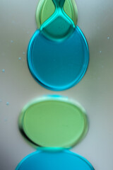 Vibrant green droplet encased in a blue fluid form, set against a neutral background with tiny...
