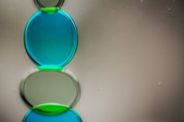 Vibrant green droplet encased in a blue fluid form, set against a neutral background with tiny...